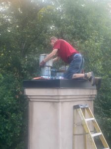 a man is kneeling on top of a chimney next to a ladder .