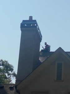 a man is sitting on top of a roof cleaning a chimney .